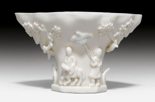 A BLANC DE CHINE VESSEL IN THE FORM OF A RHINOCEROS HORN CUP WITH FIGURES AMONG PRUNUS IN HIGH RELIEF.