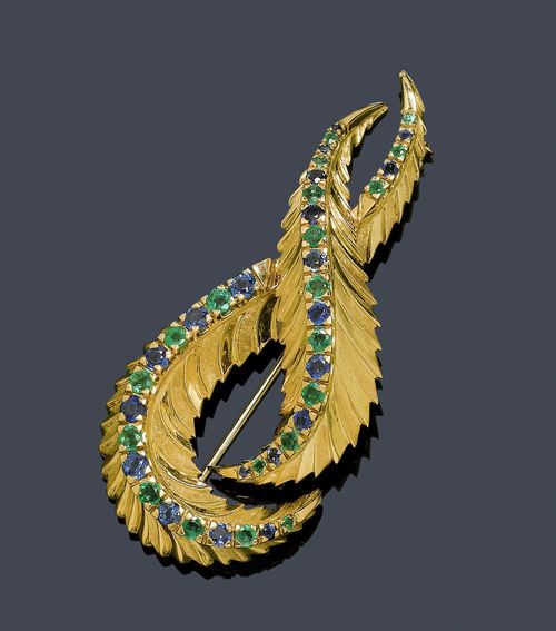 SAPPHIRE AND EMERALD BROOCH, ca. 1950. Yellow gold 750, 26g. Elegant brooch designed as two stylized leaves with a structured and partially finely satin-polished surface, the centre line set throughout with 20 sapphires weighing ca. 0.60 ct, and 19 emeralds weighing ca. 0.40 ct, respectively. L ca. 6.2 cm.