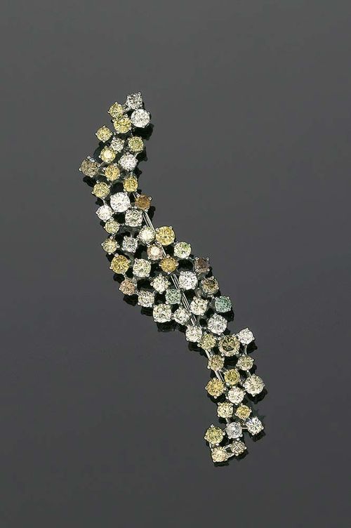 BRILLIANT-CUT DIAMOND BROOCH. White gold 750. Attractive elongated, curved brooch, completely set with 55 brilliant-cut diamonds, in white, fancy yellow - fancy brownish and 1 light-blue brilliant-cut diamond totalling ca. 5.10 ct. Matches the following lots.