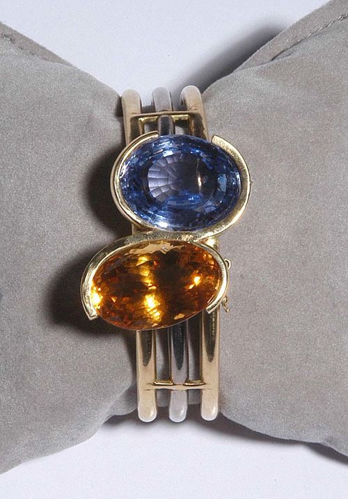 SAPPHIRE AND CITRINE BANGLE, ca. 1950. White and yellow gold 750. Casual and fancy bicolour bracelet consisting of 3 gold bracelets attached to one another, the top is decorated with 1 large oval citrine of ca. 30.00 ct, and 1 large oval Ceylon sapphire of ca. 38 ct. Ca. 6 x 5.5 cm.