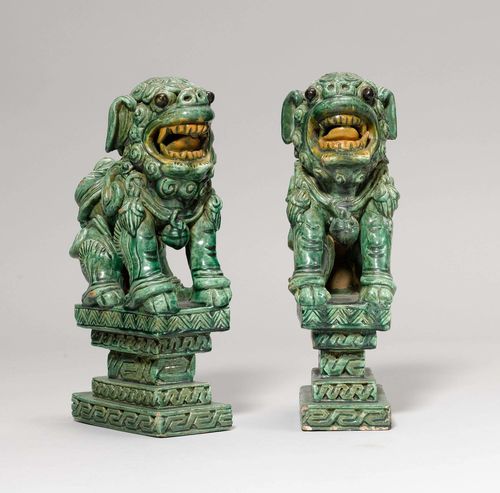 PAIR OF FO DOGS.China, Qing dynasty, H 30.5 cm. Pottery with green glaze. The dogs crouch dynamically with wide open mouths on five-tiered plinths. Some wear. (2)